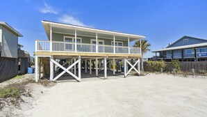 A beachfront house with a balcony, a number '316' on the front, and a sandy ground.