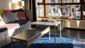 A modern living room with a large window, a sofa, a coffee table, and a lamp. - Luxury Apartment in Balkan Breeze 7 in Sunny Beach (Sunny Beach)