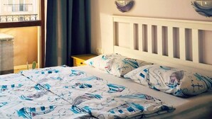 A bedroom with a bed, a window with curtains, a wall-mounted painting, and a radiator. - Luxury Apartment in Balkan Breeze 7 in Sunny Beach (Sunny Beach)