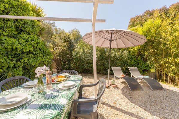 An outdoor dining area with a table set for two, surrounded by chairs, a large umbrella, and a gravel path. - Auguière West, house in the heart of the vineyard (Hyères)