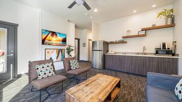 A modern living room with a sofa, coffee table, and a kitchen area with a refrigerator and microwave.