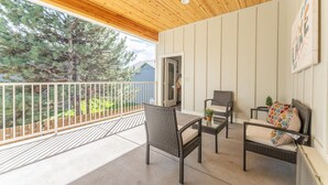 A covered balcony with wicker furniture, a white railing, and a view of trees and a house. - The Lodge Lake Chelan (Manson)