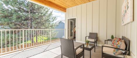 A covered balcony with wicker furniture, a white railing, and a view of trees and a house.
