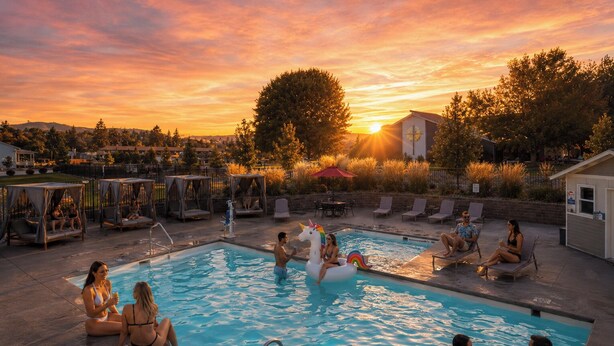 A swimming pool with lounge chairs, a small building, and trees in the background. - The Lodge Lake Chelan (Manson)