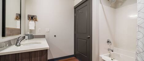 Un baño moderno con tocador de madera, un espejo grande, una puerta oscura y una bañera blanca.