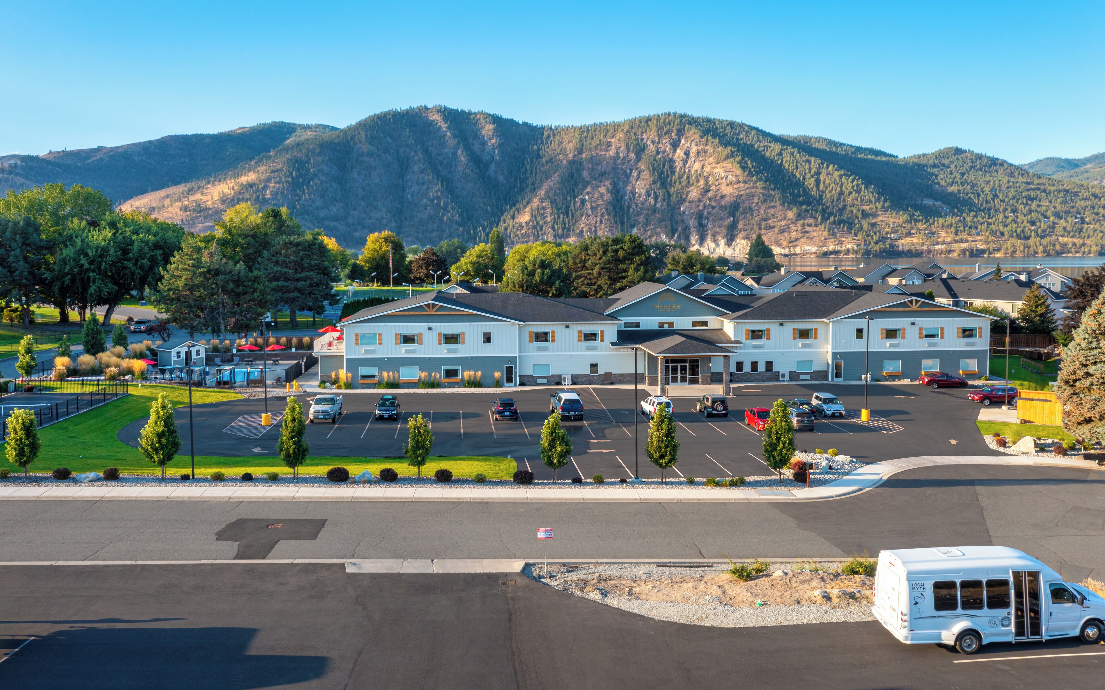 A hotel with a parking lot, a building with a sign reading "The Lodge", and mountains in the background.