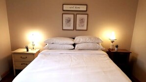 Una cama bien tendida con sábanas blancas, dos mesitas de noche con lámparas, y dos cuadros con motivos florales en la pared.