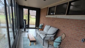 Un patio amplio con pared de ladrillo, un sofá gris, un banco de madera y una silla de mimbre.