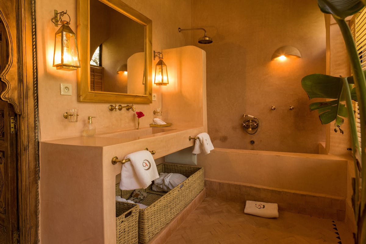 A bathroom with a bathtub, a sink with a mirror, and wall-mounted lights. There are wicker baskets under the sink and a towel rack with a towel hanging.