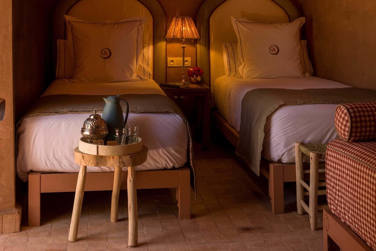 A cozy room with two beds, a small table with a teapot and glasses, and a hanging light fixture.