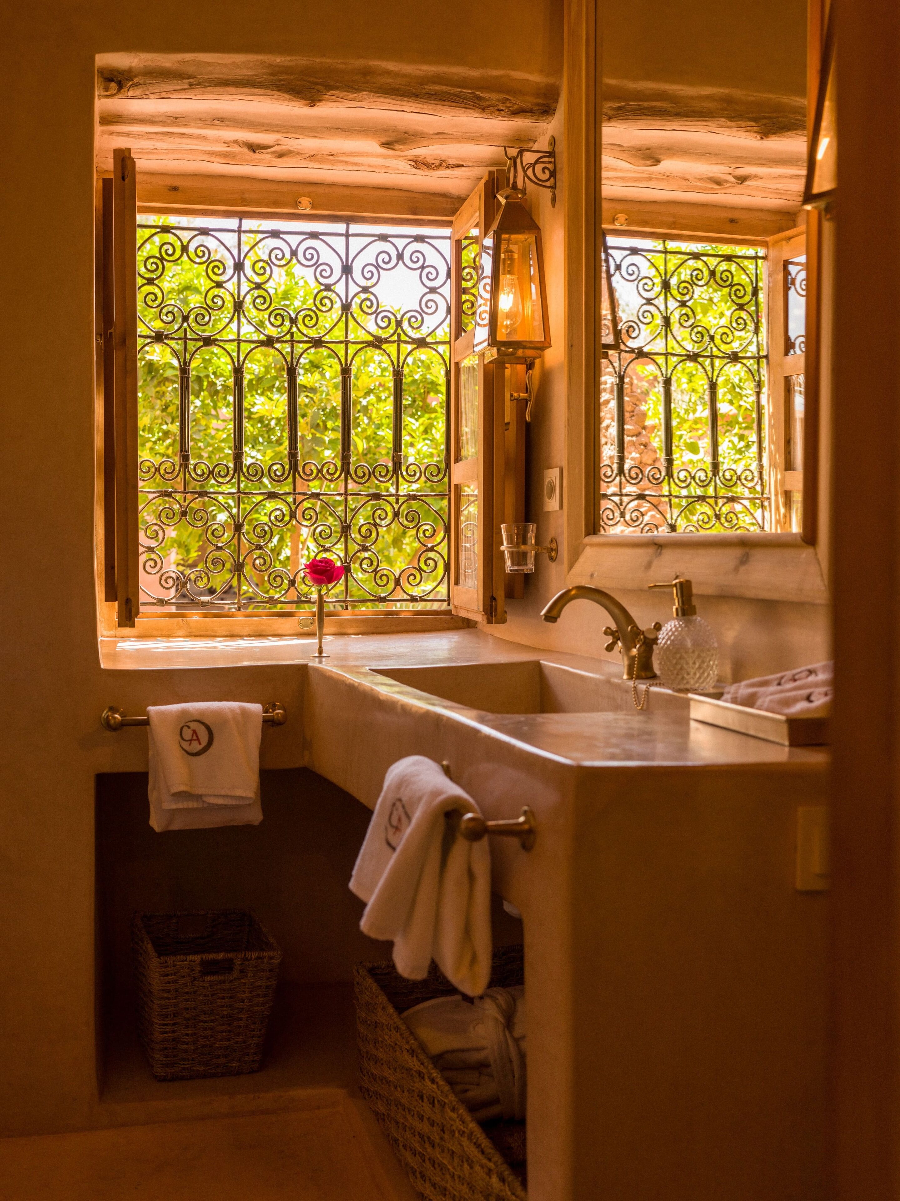 Une salle de bain avec un plafond en bois, une fenêtre ornée de barreaux en fer forgé, un lavabo et un miroir.