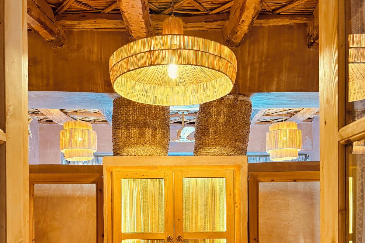 A wooden room with a large wooden door, two beds with striped bedding, and a hanging wicker chandelier.