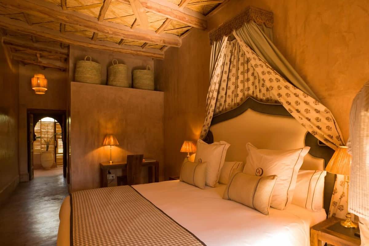 A bedroom with a large bed, two bedside tables with lamps, a canopy bed, and a view of a hallway with baskets on a shelf.