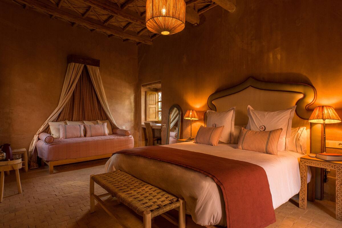 A cozy bedroom with a large bed, a bench, a daybed with curtains, and two bedside tables with lamps.