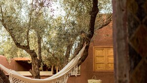 A hammock between trees, a lounge chair, and a rustic building with a wooden door. - Casa Abracadabra (Marrakech)
