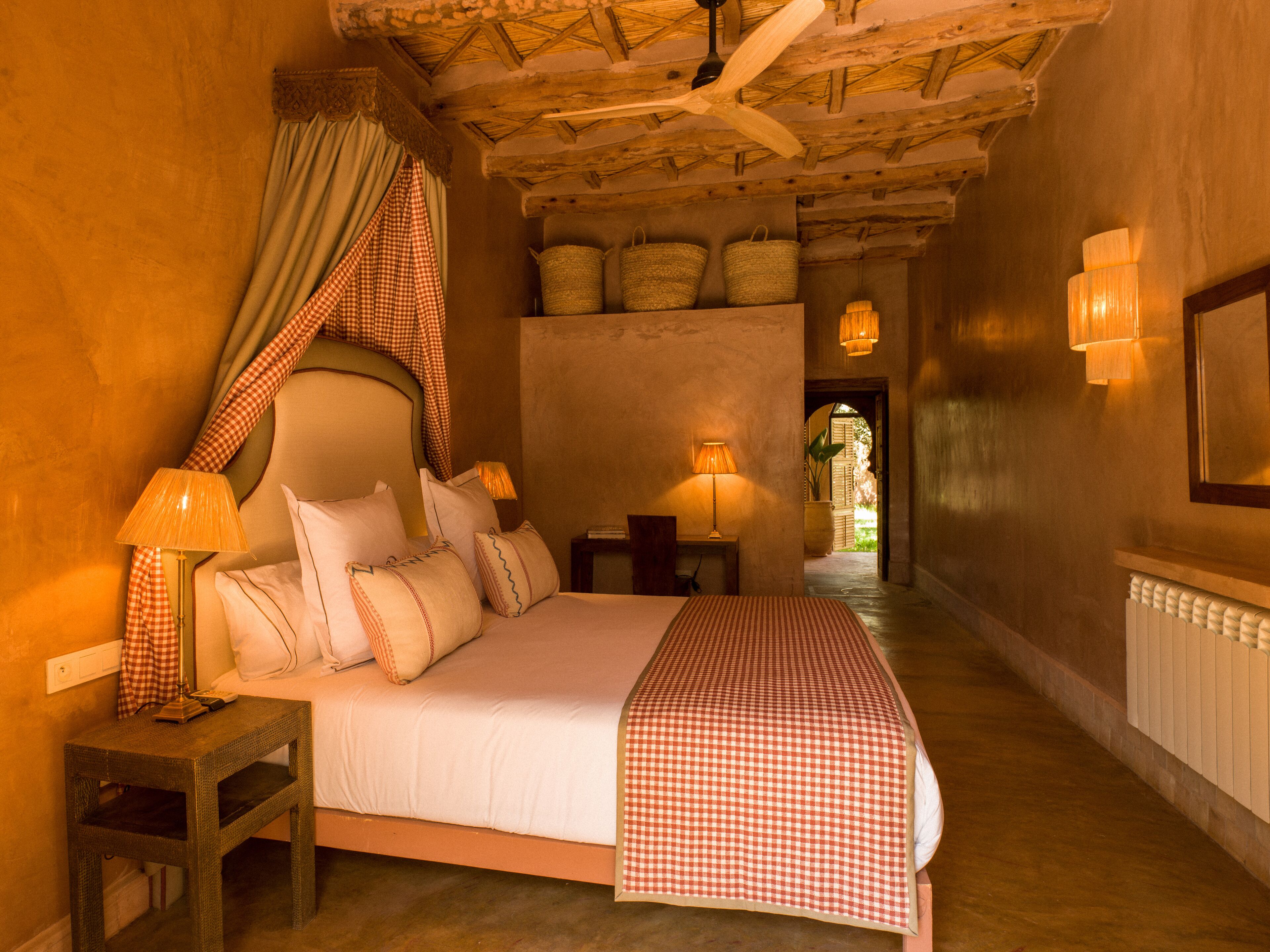 A cozy bedroom with a bed, checkered curtains, a ceiling fan, and a nightstand with a lamp.