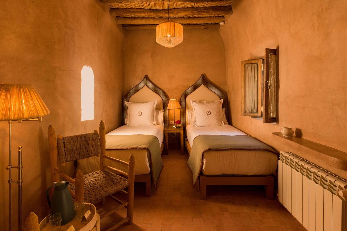 A cozy room with two beds, a wooden chair, a table with a kettle, and a radiator.