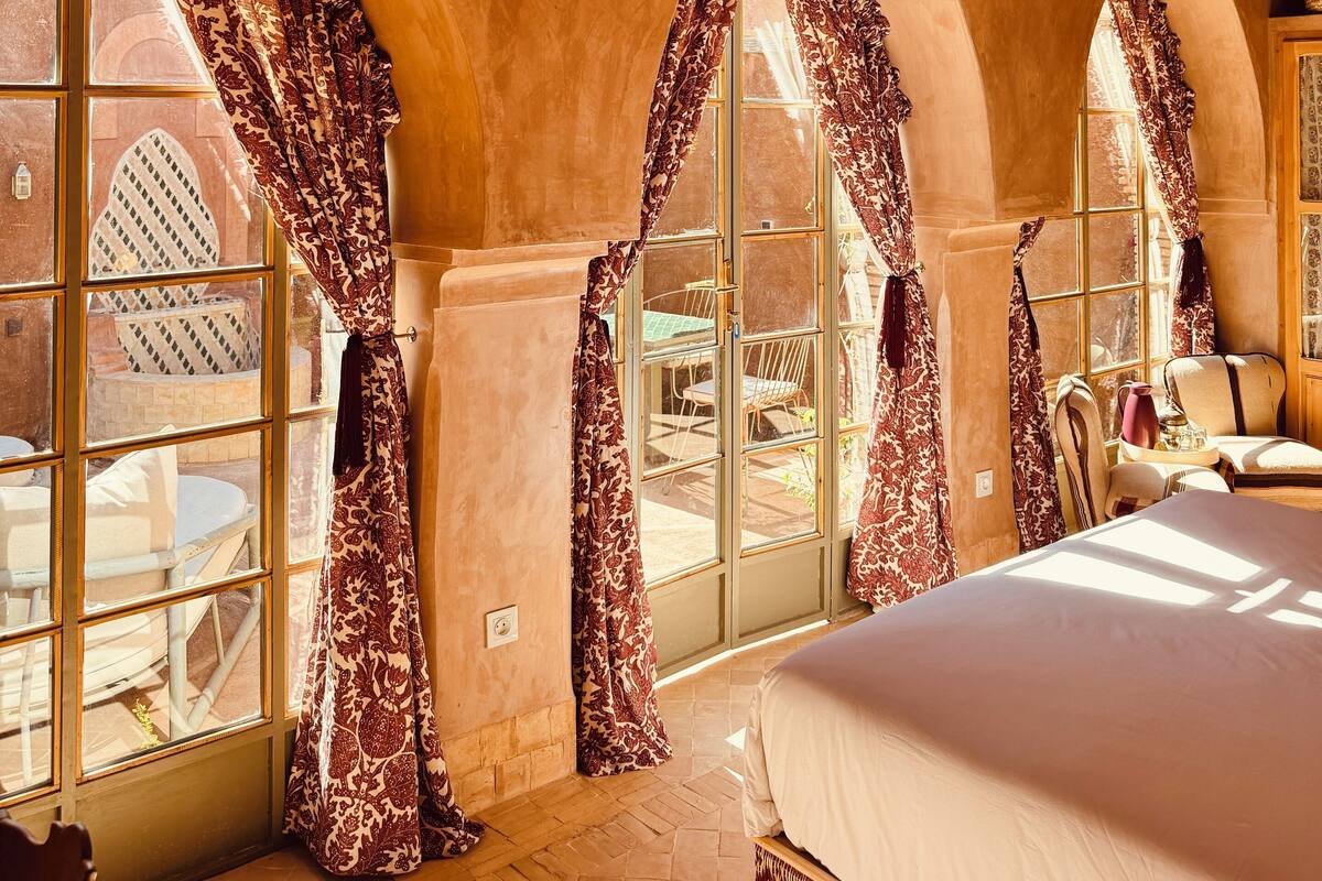 A bedroom with a large bed, arched windows, and a wooden ceiling.