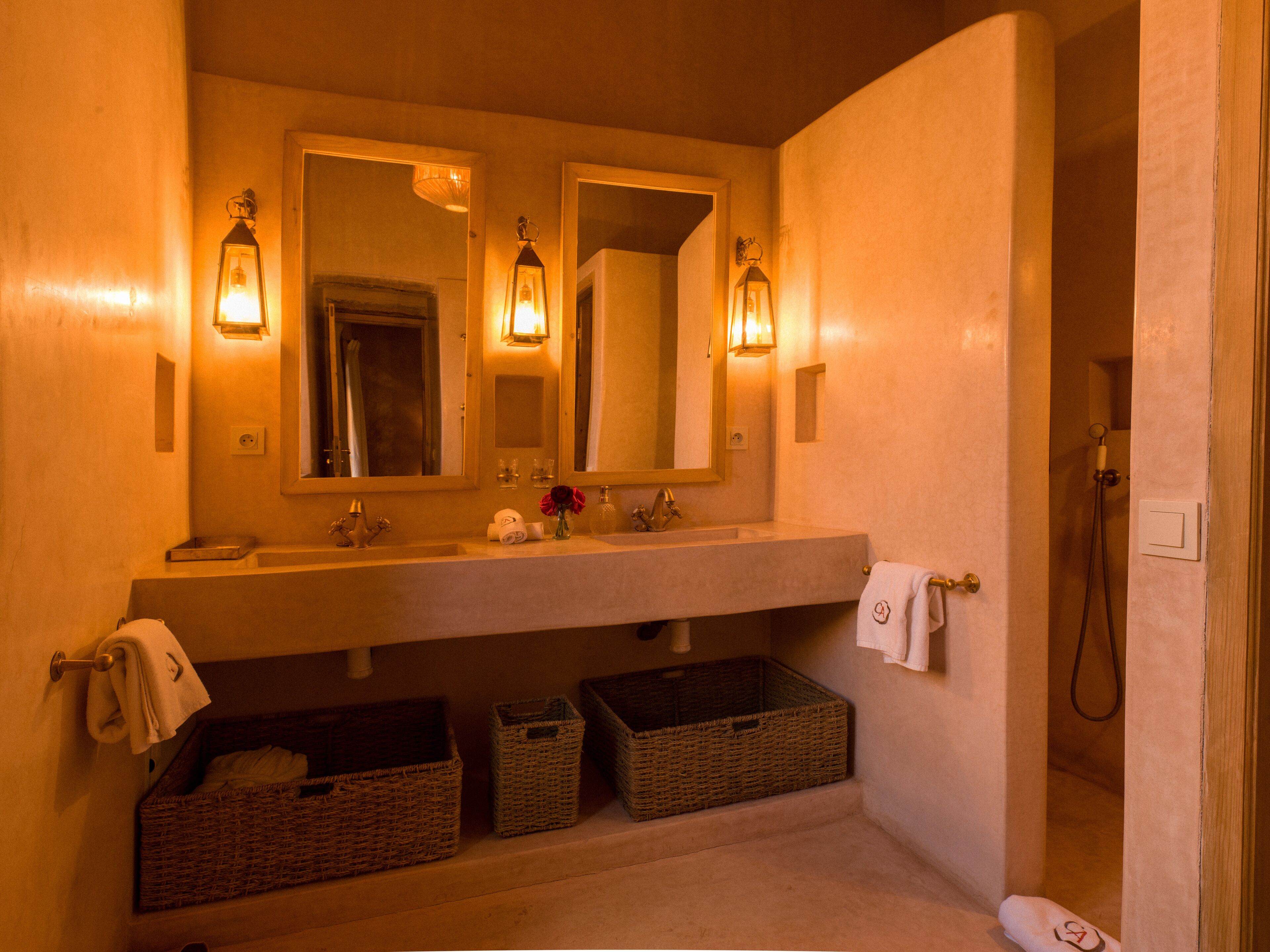 A bathroom with a large mirror, two wall-mounted light fixtures, a sink, and three wicker baskets under the counter.