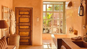 A spacious bathroom with a wooden door, a large window, a bathtub, and a sink. - Casa Abracadabra (Marrakech)