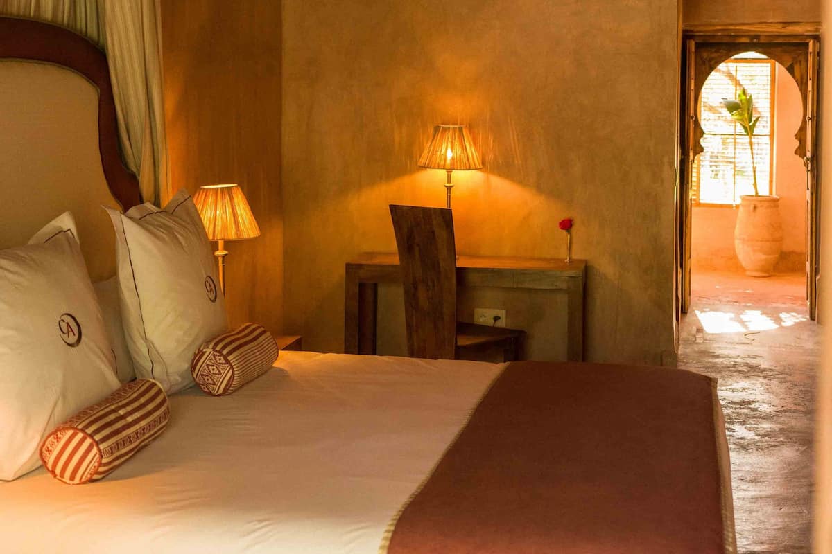 A cozy bedroom with a bed, pillows, a nightstand, a lamp, and baskets on a shelf.