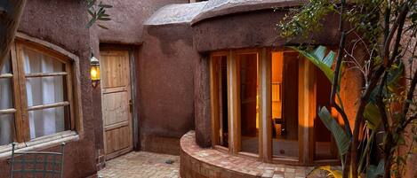 A rustic building with a tiled courtyard, a wooden door, and a window with a metal frame.