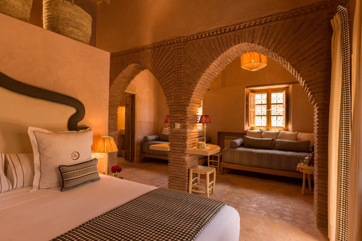 A cozy room with a large bed, a sofa, and a small table. There are arches and a window with a view.
