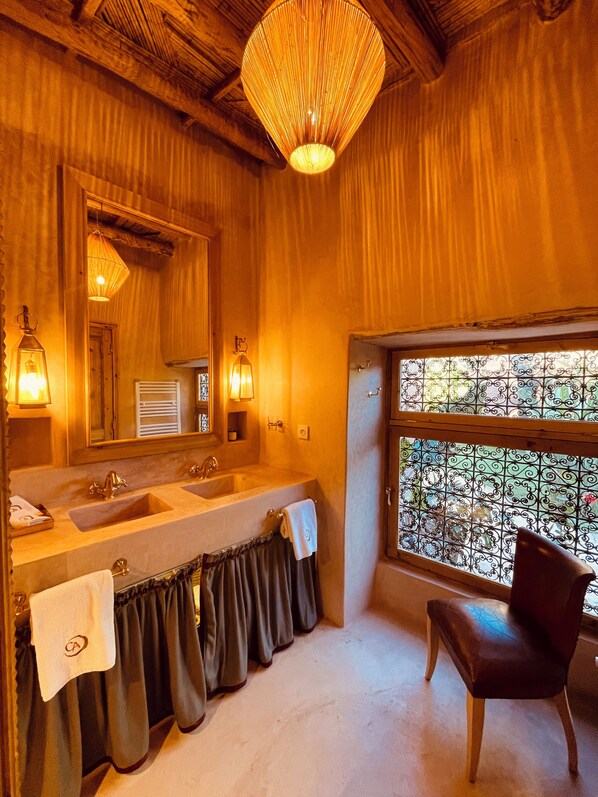 Un baño de madera con un amplio tocador, dos lavamanos, un espejo y una ventana con barandillas de hierro decorativas.