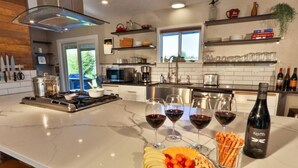 Una cocina moderna con encimera de mármol, copas de vino, una botella y una bandeja de frutas.