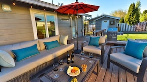 Terraza al aire libre con sofá, sillas y una mesa dispuesta con copas de vino y aperitivos.