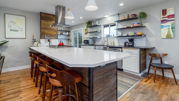 Una cocina moderna con una isla central, taburetes de bar, un microondas y una cafetera.