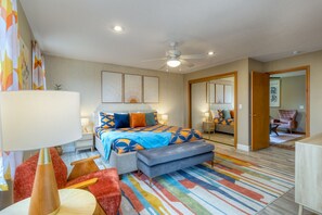 A modern bedroom with a bed, bedside tables, a ceiling fan, and a colorful rug.