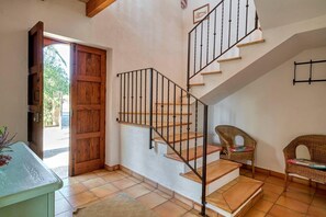 Staircase with a metal railing and wooden steps, leading to a room with a tiled floor and wicker furniture.