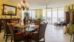 A spacious dining area with a glass-top table, wicker chairs, and a chandelier.