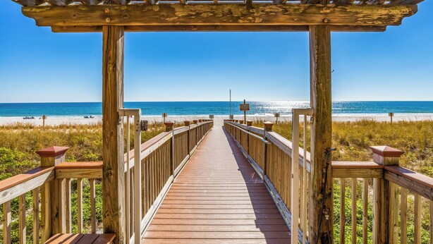 A wooden boardwalk leading to a beach with a wooden pergola overhead.