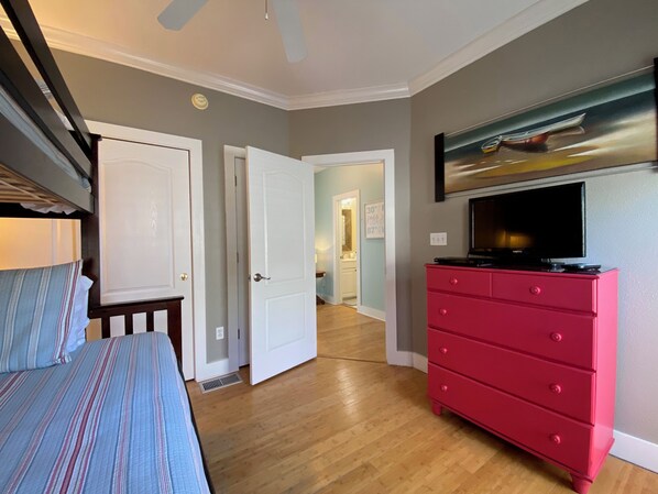 A bedroom with a bed, a red dresser, a television, and a hallway leading to another room.