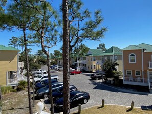 A parking lot with several cars, a building with a green roof, and a tree in the foreground.