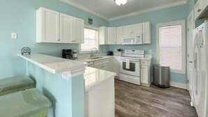 A kitchen with white cabinets, a microwave, an oven, a sink, and a trash can. - Exquisite Condo Retreat, Lagoon Oasis Pool & Pristine Beaches: No Problem (Pensacola)