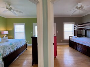 A bedroom with a bed, a dresser, a nightstand, a ceiling fan, and a window with blinds.