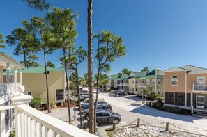 A row of two-story buildings with balconies, a parking area with cars, and a clear blue sky.