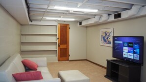Una sala de estar con un sofá blanco, almohadas rojas, un mueble de entretenimiento negro y un televisor que muestra servicios de transmisión.