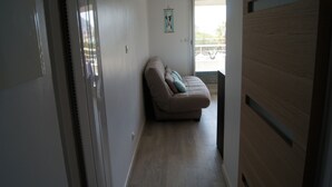 Een smalle gang met een beige bank tegen de muur, een houten vloer en een deur aan de linkerkant.