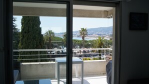 Een balkon met uitzicht op een kustplaatsje, een palmboom en een hoge naaldboom.