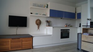 Een moderne keuken met witte kasten, een ingebouwde oven en een flatscreen tv aan de muur.