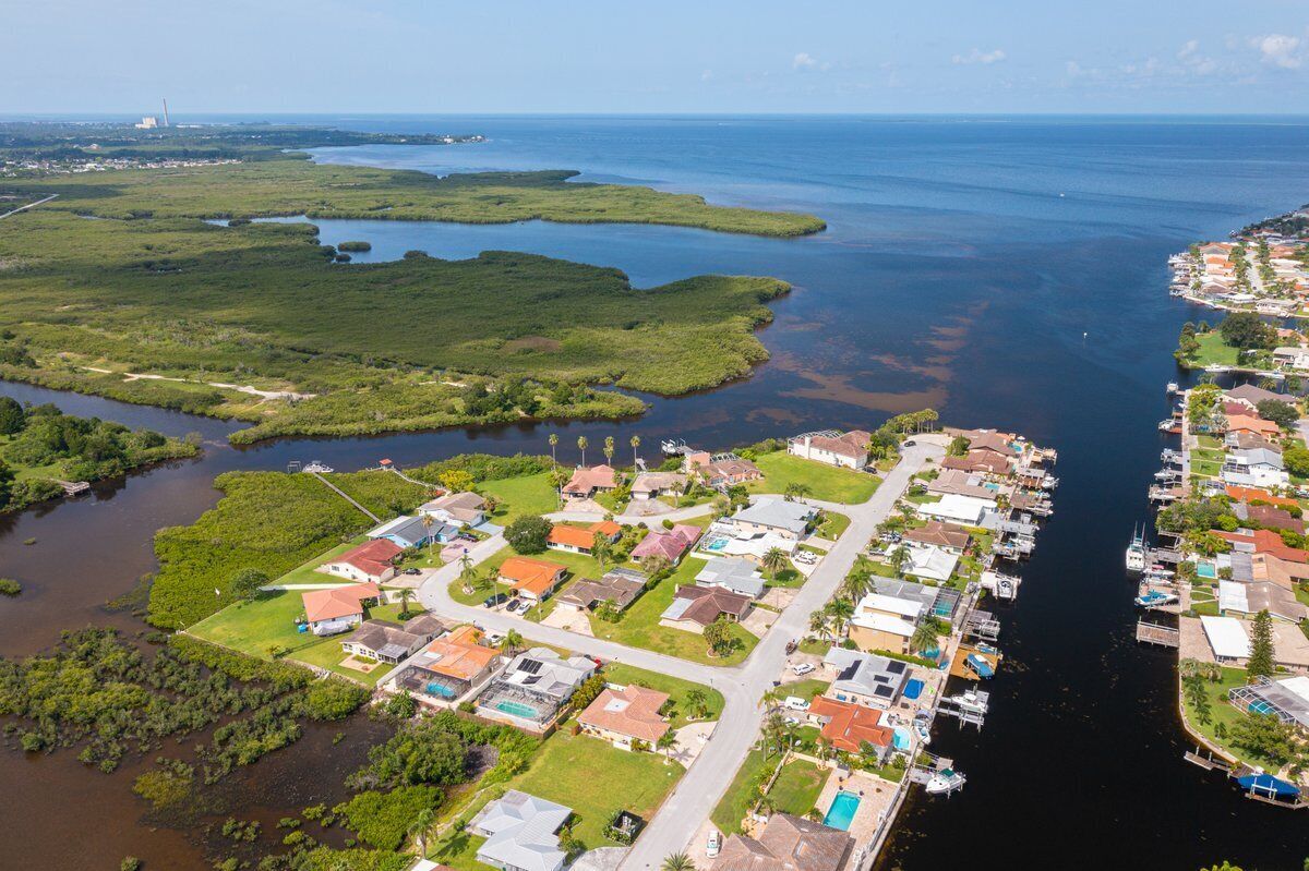 An aerial view of a coastal residential area with houses, a marina, and adjacent mangrove areas.