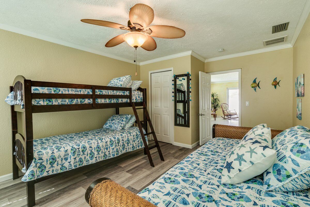 A room with bunk beds, a ceiling fan, and a door leading to another room.