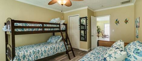 A room with bunk beds, a ceiling fan, and a door leading to another room.