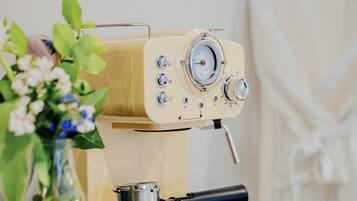 A vintage espresso machine on a wooden table with a small metal pot and a glass vase with flowers.