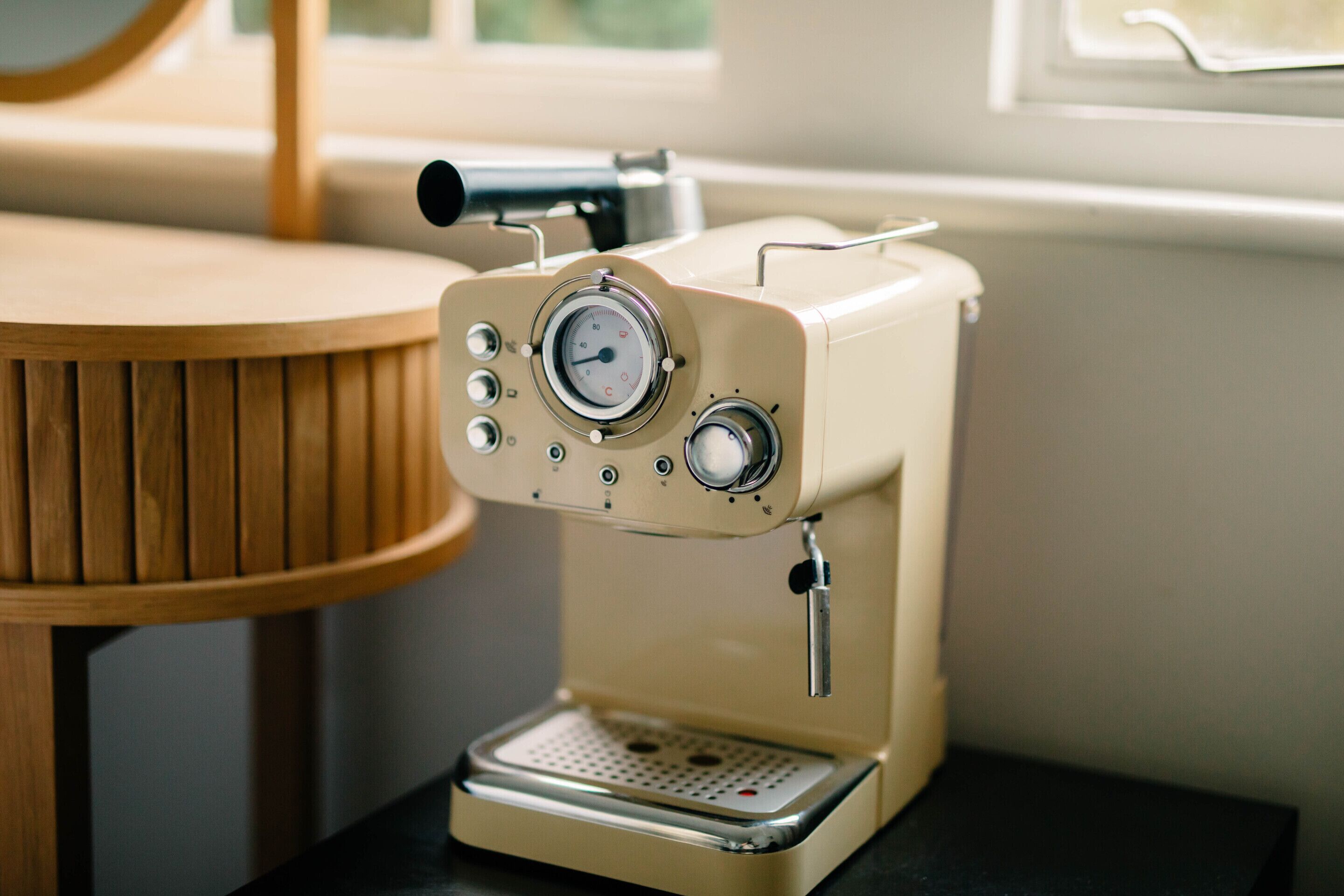 A vintage espresso machine with a dial, buttons, and a coffee pot on a table.