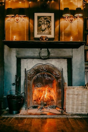 A fireplace with a decorative screen, a framed picture above it, and a wicker basket to the right. - The Ram Inn (Lewes)